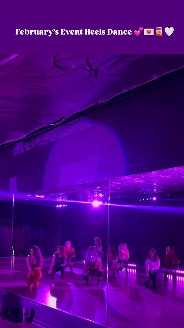 A group of dancers crouched low in a violet-lit mirrored studio